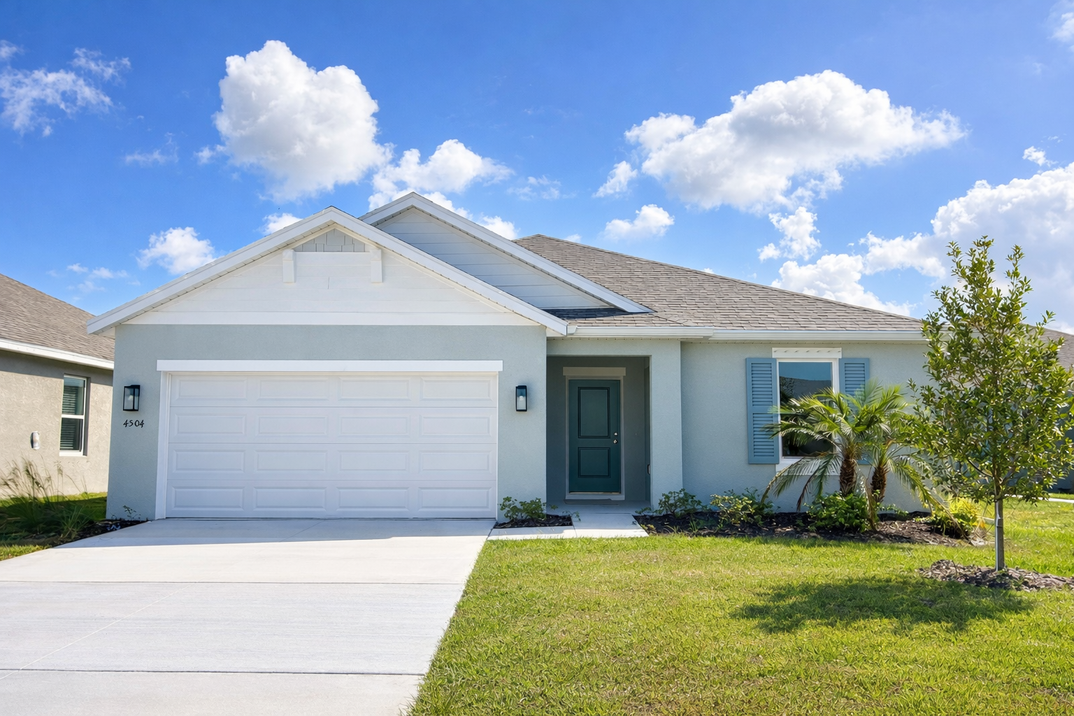 new construction single-family home featuring a two-car garage, pale blue exterior, and tropical landscaping